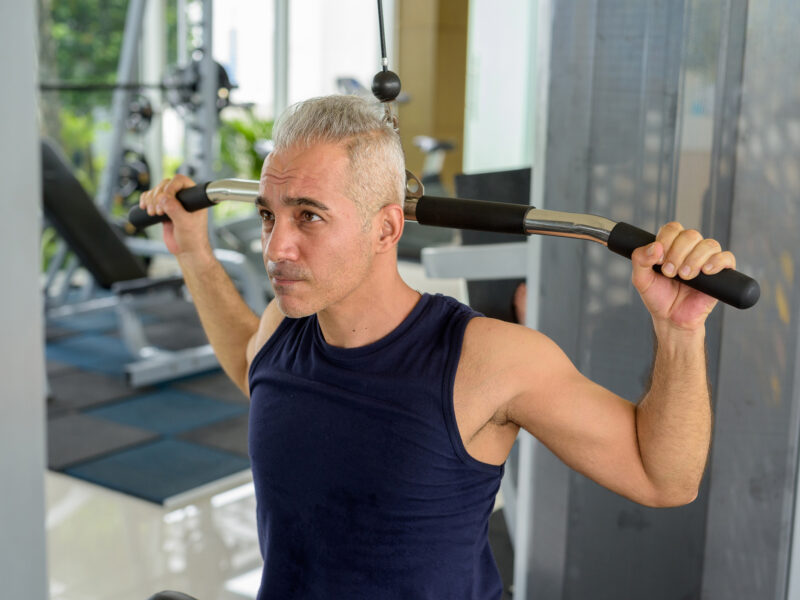 Mature handsome Persian man using pull down machine at the gym